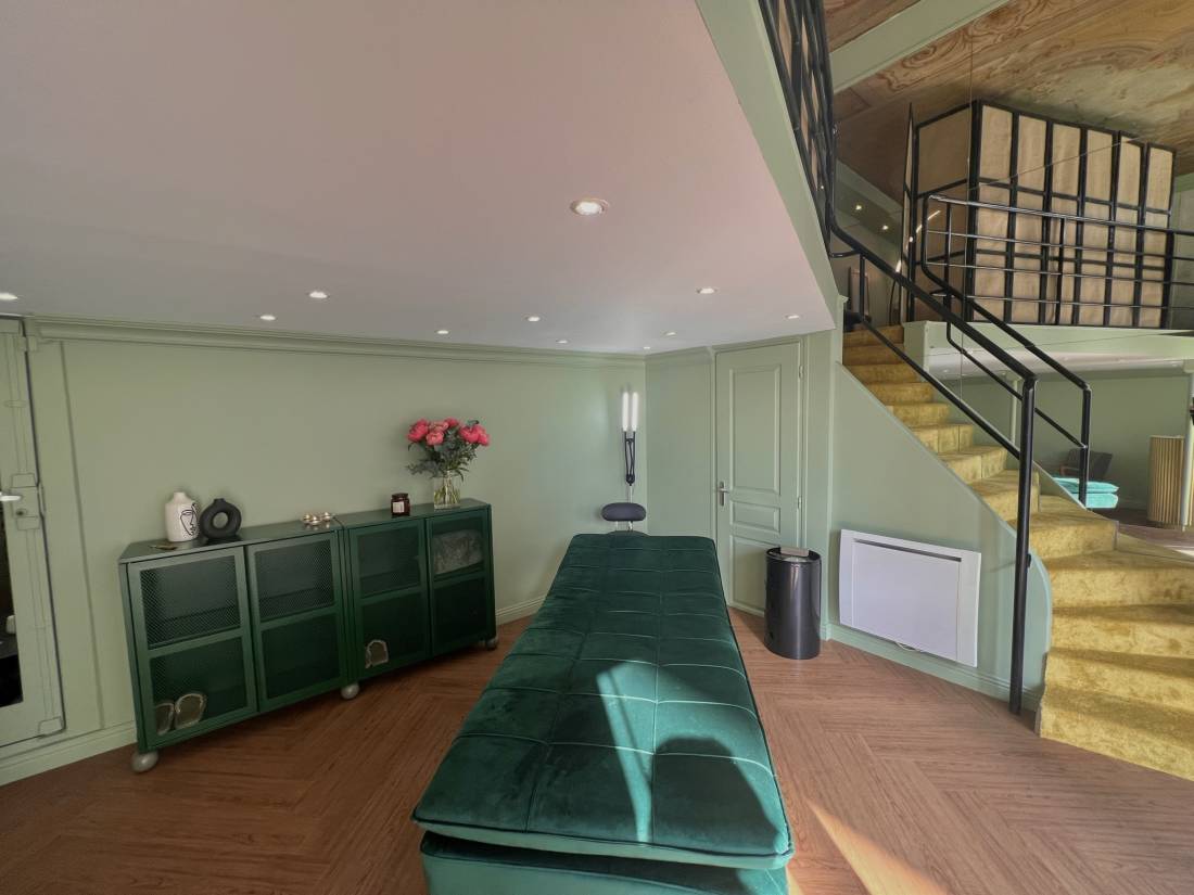 La cabine de soin d'ÔVA essentiel : murs vert sauge, banquette en velours vert et escalier doré